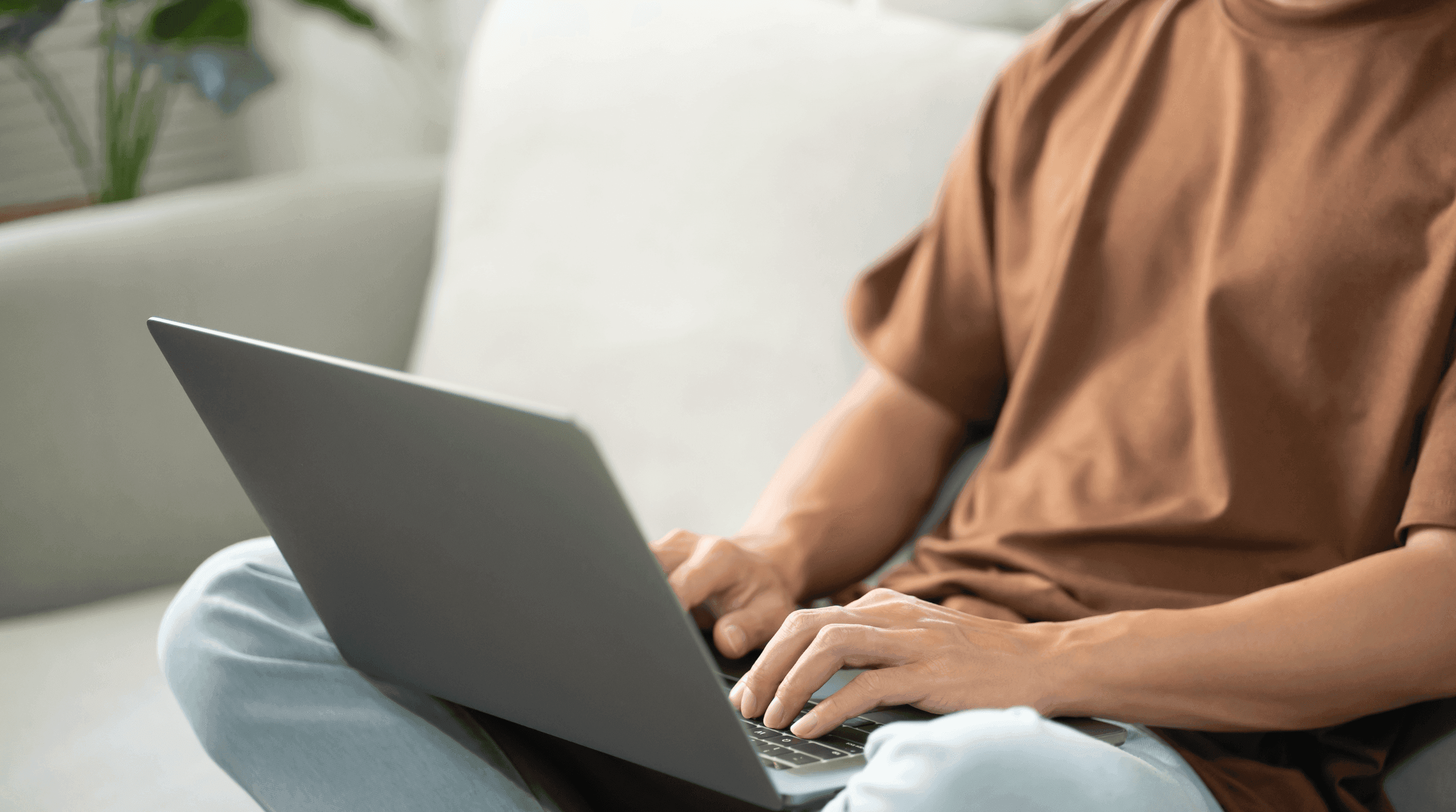 Person sitz mit Laptop auf dem Schoss auf einer Couch
